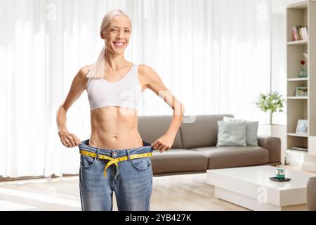 Donna sottile e felice in un paio di jeans grandi e top in crescita in salotto Foto Stock