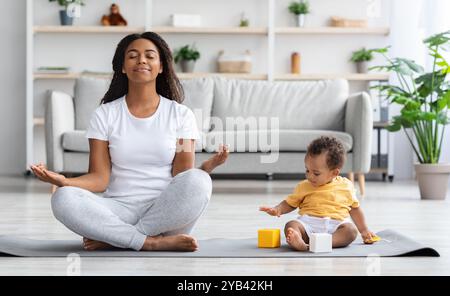 Concetto di benessere mentale. Calma Happy Black Madre meditando con il bambino a casa Foto Stock