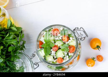 Insalata di couscous fresca in un vaso di vetro con cetrioli, pomodori, erbe aromatiche, limone con ingredienti su sfondo bianco. Insalata di tabbouleh. Vegetariano sano Foto Stock