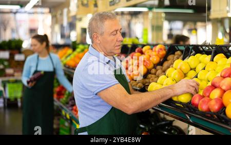 Uomo anziano concentrato in grembiule che prepara mele Golden Delicious nella sezione frutta Foto Stock