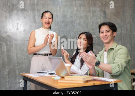 Un gruppo di giovani membri del team di startup asiatiche batte le mani, applaude per celebrare il successo del loro business e sorride alla telecamera. affari Foto Stock