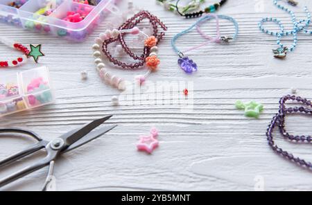 Varie perline, ciondoli e strumenti sono sparsi su un tavolo di legno mentre un artista disegna pezzi unici di gioielli in una vivace sessione di lavorazione. Foto Stock