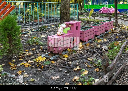 Un affascinante trenino giocattolo in legno rosa sorge nel giardino del parco, progettato come parte di un'installazione decorativa giocosa Foto Stock