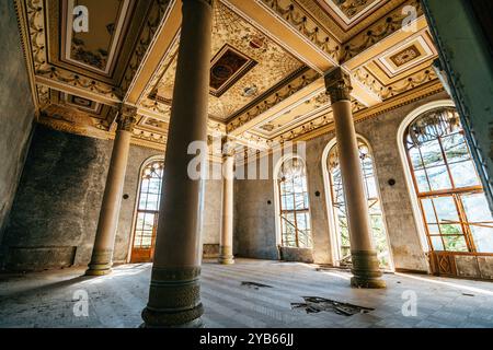 Sala da ballo vuota e decadente, caratterizzata da colonne alte, finestre ad arco e intricati soffitti in un edificio storico abbandonato. Foto Stock