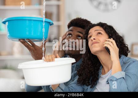 giovane coppia emotiva che raccoglie le perdite d'acqua dal soffitto Foto Stock