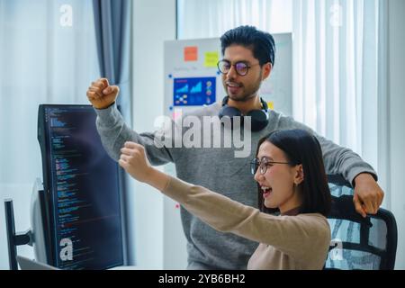 Il team di sviluppatori asiatici e indiani batte la mano per il successo del progetto con un computer software in ufficio Foto Stock