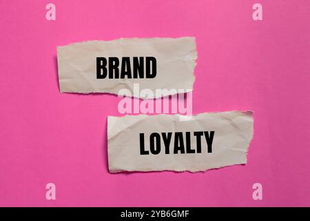 Messaggio di fedeltà al marchio scritto su pezzi di carta strappati con sfondo rosa. Simbolo concettuale di fedeltà al marchio. Copia spazio. Foto Stock