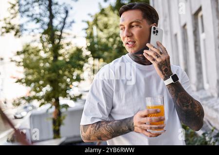 Un giovane elegante si trova all'aperto, parla al telefono e si sorseggia un drink rinfrescante. Foto Stock