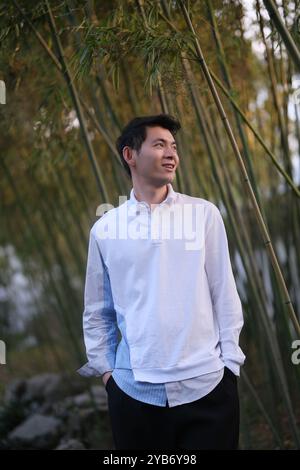 Sorridi bel giovane asiatico, mani in tasca, al boschetto di bambù Foto Stock