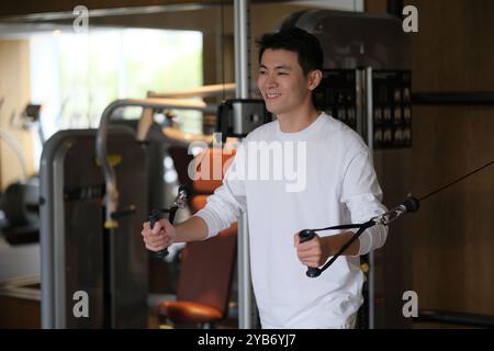 Sorridi giovane asiatico allenarsi con la macchina kinesis in palestra Foto Stock