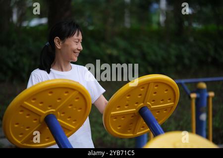 Una vecchia donna cinese sorridente si allena con l'attrezzatura fitness all'aperto. Stile di vita sano Foto Stock