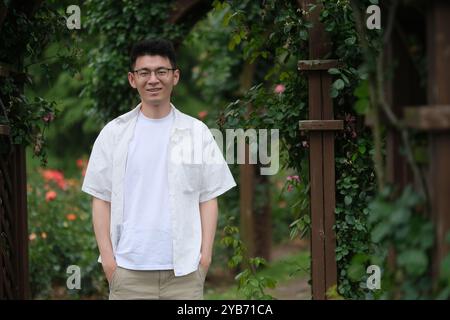 Sorridente giovane asiatico al giardino verde. Primo ritratto di un uomo cinese in estate Foto Stock