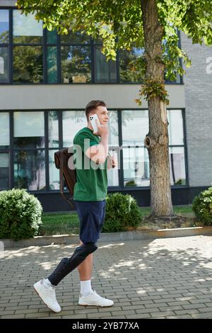 Un giovane e affascinante uomo con una gamba protesica cammina con sicurezza mentre parla al telefono. Foto Stock