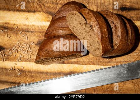 Una pagnotta di pane di segale con aggiunta di malto, tagliata a metà su un asse di legno con un coltello speciale. Il concetto di arricchimento del pane con specialità Foto Stock