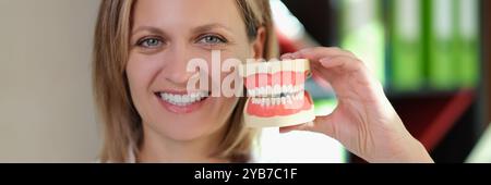 Il dentista tiene il modello realistico delle mascelle vicino al volto sorridente Foto Stock