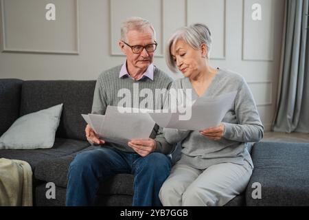 Triste stanco, deluso, coppia di anziani di mezza età siedono con un documento cartaceo. Infelice anziano maturo donna che legge banconote che gestiscono le finanze bancarie calcolano le tasse pianificazione prestito pagamento pensione Foto Stock