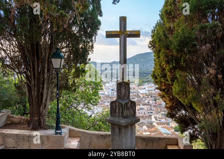 Scultura di una croce di pietra nel Calvario della città di Arta, con la città sullo sfondo all'alba. Isole Baleari, Spagna Foto Stock