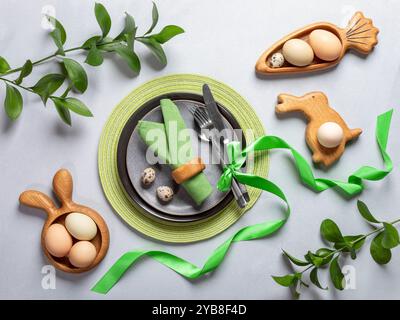 Vista dall'alto alla tavola di Pasqua. Ambiente di vacanza dai colori naturali. Piatti rotondi e figurati, tovaglioli verdi e nastro, uova biologiche, posate, primavera Foto Stock