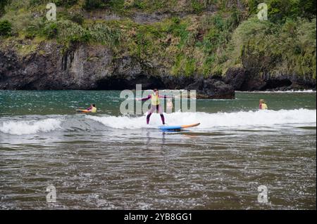 Una giovane surfista salta in equilibrio sulla sua tavola mentre cavalca una piccola onda durante una sessione di scuola di surf sulla spiaggia di Seixal Foto Stock