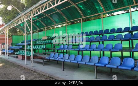 sedie di plastica blu e verdi sotto un baldacchino verde, un frammento di uno spettatore all'aperto senza visitatori, luoghi per guardare le corse di cavalli Foto Stock