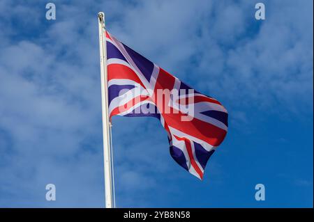 L'Union Jack fluttua orgogliosamente in cima a un'asta di bandiera sullo sfondo di un cielo blu vibrante pieno di soffici nuvole bianche, catturando una giornata luminosa Foto Stock