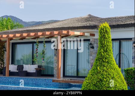 Questa splendida villa sfoggia un'architettura moderna combinata con elementi naturali, circondata da una vegetazione vibrante e montagne sotto un cielo azzurro Foto Stock