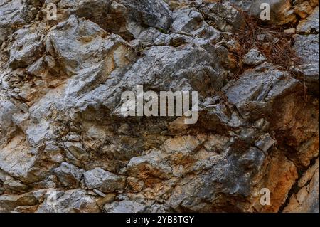 La superficie ruvida di una grande formazione rocciosa mostra una miscela di sfumature grigie e marroni, evidenziando le texture naturali formatesi nel tempo in una montagna Foto Stock