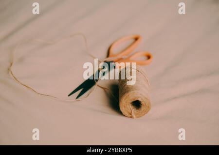 Sul tessuto beige è presente una bobina di corda di canapa e un paio di forbici moderne. Questo è un processo di produzione. E' un hobby. Foto Stock