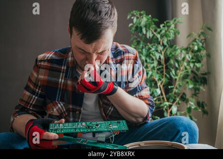 Il tecnico che indossa i guanti sta ispezionando una scheda di circuito, cercando di individuare la causa del problema mentre è seduto sul pavimento Foto Stock