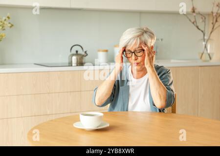 Mal di testa. Donna anziana infelice di mezza età che soffre di mal di testa malata che sfrega le tempie a casa. Anziana nonna anziana matura che tocca i templi che sperimenta stress donna che sente dolore alla testa Foto Stock