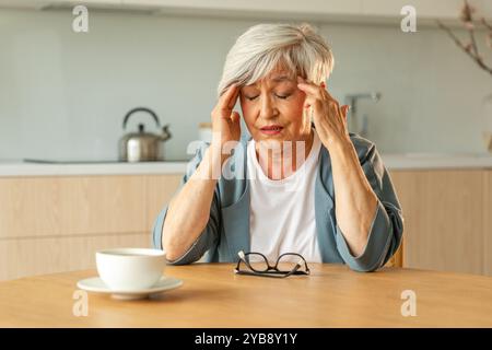 Mal di testa. Donna anziana infelice di mezza età che soffre di mal di testa malata che sfrega le tempie a casa. Anziana nonna anziana matura che tocca i templi che sperimenta stress donna che sente dolore alla testa Foto Stock