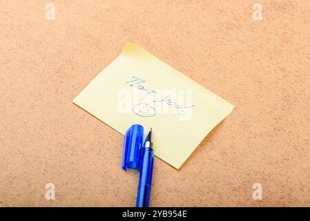 Una nota scritta a mano che dice "grazie" con una faccia sorridente, posta su uno sfondo di legno. Foto Stock