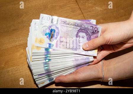 Una persona in possesso di una grande pila di banconote da 20 libbre, che mostra i colori vivaci e i disegni intricati della valuta. Le funzioni di sfondo Foto Stock