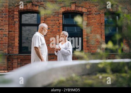 Un'ampia foto di una coppia di anziani felici in piedi sulla strada della città e in pausa caffè, godendosi la pensione e trascorrendo del tempo insieme con un caldo sole Foto Stock