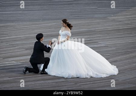 Giovane uomo giapponese che propone su un ginocchio una bella ragazza giapponese in abito da sposa sul molo di Osanbashi, Yokohama, Giappone il 24 settembre 2024 Foto Stock