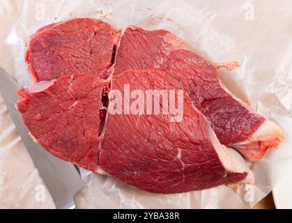 Primo piano di due tagli di filetto di manzo crudo posti su carta da forno bianca con accanto un coltello da cucina, pronti per la cottura Foto Stock