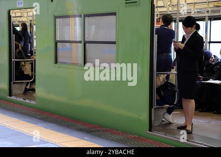 Una giovane donna in tuta che guarda il suo telefono mentre aspetta la partenza del treno.Kyoto.Giappone Foto Stock