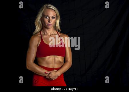 Una splendida modella atletica si posa in sicurezza in uno studio, i suoi muscoli tonificati evidenziati da un'illuminazione soffusa. Trasuda forza e grazia, mostrando Foto Stock