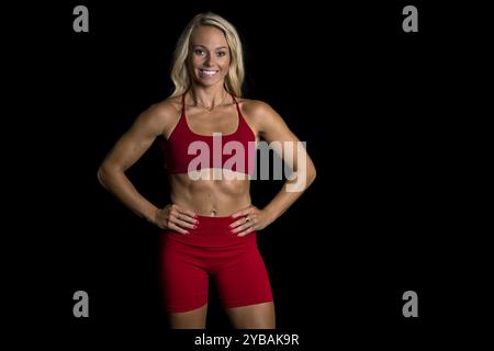 Una splendida modella atletica si posa in sicurezza in uno studio, i suoi muscoli tonificati evidenziati da un'illuminazione soffusa. Trasuda forza e grazia, mostrando Foto Stock