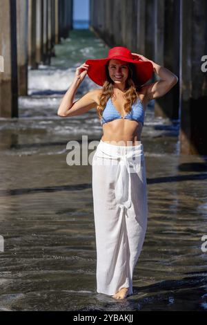 Una donna mozzafiato si crogiola nella beatitudine della spiaggia, vicino a un molo, sotto cieli azzurri, abbracciando la serenità di una giornata perfetta in riva al mare Foto Stock