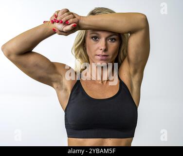 Una splendida modella atletica si posa in sicurezza in uno studio, i suoi muscoli tonificati evidenziati da un'illuminazione soffusa. Trasuda forza e grazia, mostrando Foto Stock