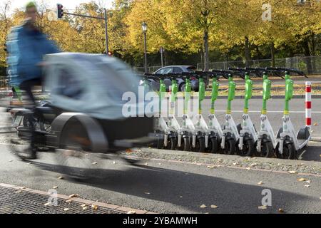 Traffico, mobilità, sfocatura del movimento, ciclista con bici da carico e scooter elettrici allineati dal fornitore Lime in autunno su una strada a Berlino, Germania, Europ Foto Stock