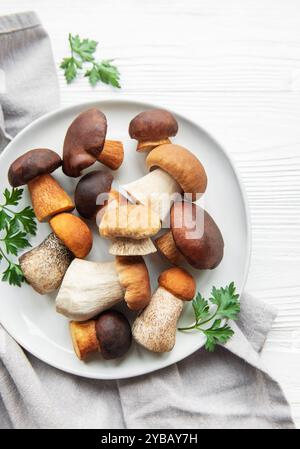 Un assortimento di funghi freschi è disposto su un piatto, mostrando forme e colori diversi, accompagnati da prezzemolo su un backgroun di legno testurizzato Foto Stock