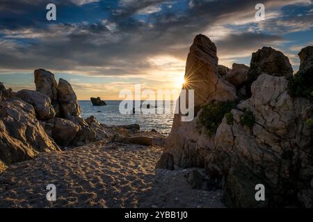 Una spiaggia rocciosa con il sole che tramonta sul mare che getta le luci sulle nuvole del cielo e il raggio del sole che sbircia dietro una roccia. Una vacanza, ecologia, ambientalisti Foto Stock