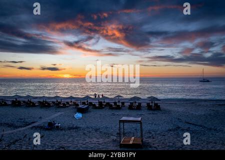 Kathisma Beach, isola di Lefkada, Grecia, con lettini, ombrelloni, e i turisti che si godono gli splendidi ultimi raggi del sole mentre il sole tramonta sotto il mare horizo Foto Stock