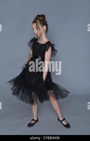 Una giovane ragazza tiene con grazia l'orlo del suo abito nero, mostrando i suoi strati di tulle fluenti. Questa immagine mette in risalto l'eleganza e il fascino dei bambini Foto Stock