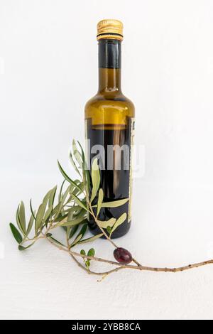 Vista laterale di una bottiglia di olio d'oliva con oliva nera su un ramo, isolata su sfondo bianco, Foto Stock