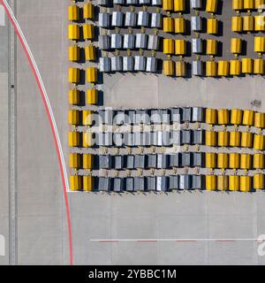 Vista dall'alto dei carrelli per bagagli gialli e neri vuoti in fila sulla soleggiata asfalto dell'aeroporto Foto Stock