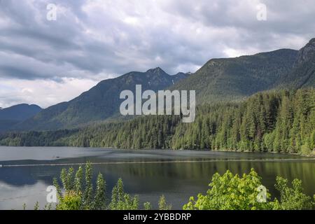 Una vista panoramica del lago calmo con lo sfondo di montagne lussureggianti e boscose e cieli ricoperti al Capilano River Regional Park Foto Stock