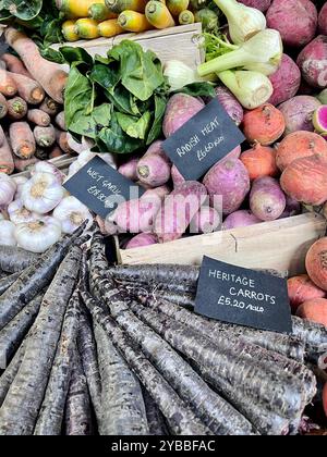 Verdure fresche di stagione autunnali presso un mercato agricolo con il nome e i prezzi sull'ardesia nera. Carote viola, patate dolci, aglio, finocchio. Foto Stock